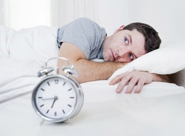 A Man Trying To Sleep In Front Of An Alarm Clock