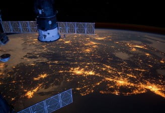 An image of space craft in the space with a stunning view of night lights on earth
