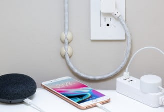 A photo of iPhone 8 Plus with Google Home Mini and a power extension plugged in socket showing smart and secure home