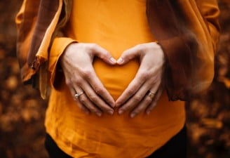 A photo of husband and pregnant wife making heart with hands